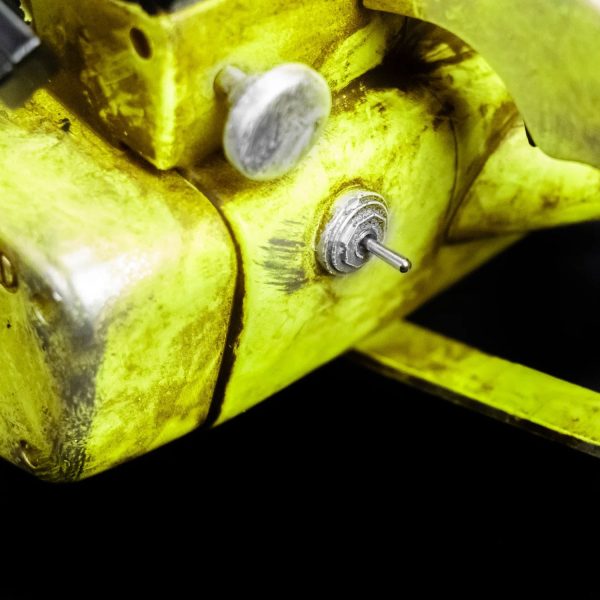 Close-up of a metal toggle switch and silver knob on a weathered yellow machine
