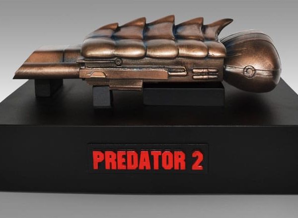 Bronze-colored Predator 2 prop replica on a black display base with a red logo