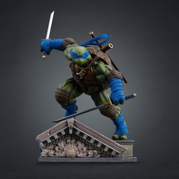 Leonardo TMNT statue in a crouched battle pose on a stone rooftop base, wielding two katanas