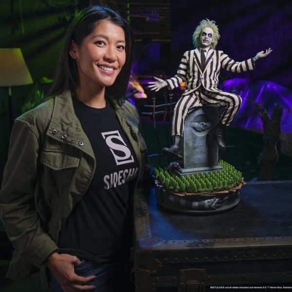 A woman stands next to a Beetlejuice collectible figure sitting on a tombstone to show its scale